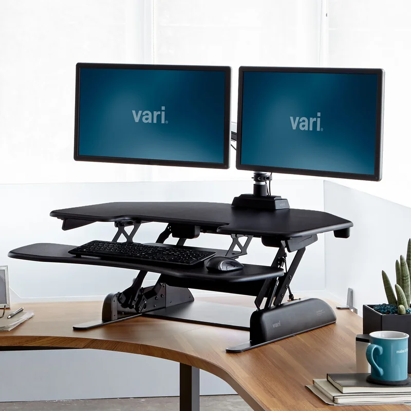 VariDesk dual monitor standing desk converter raised to standing height on a wooden home office desk
